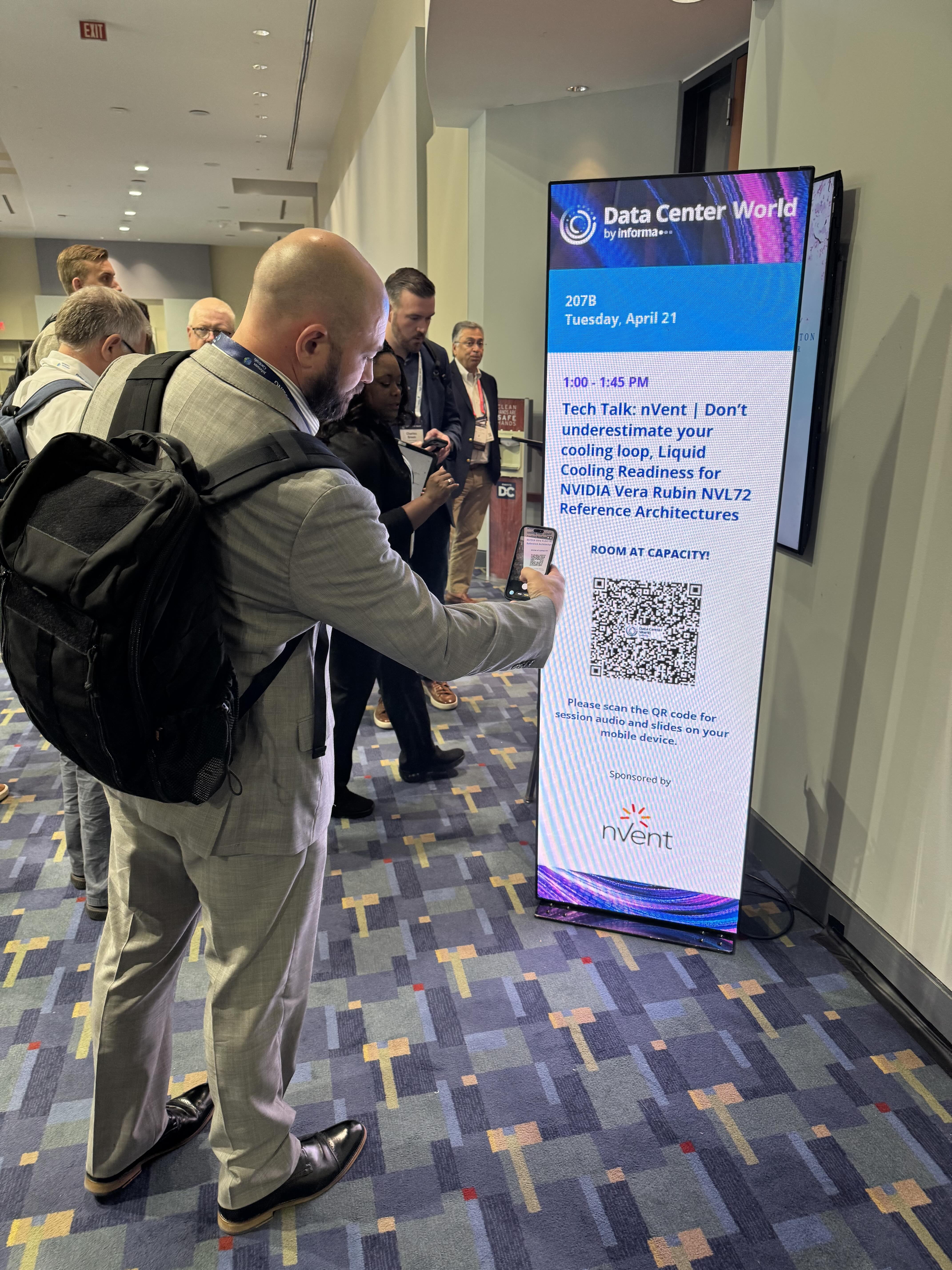 Attendee scanning a QR code beside a ROOM AT CAPACITY sign at Data Center World